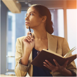 Business woman looking away holding a book in one hand and a pen in the other